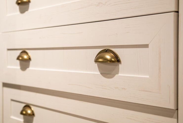 Złote uchwyty na szufladach białej drewnianej szafy